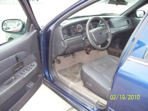 2005 Ford Crown Victoria - The interior of a blue 2005 Ford Crown Victoria is visible with the driver's side door open, showing the dashboard and front seat.