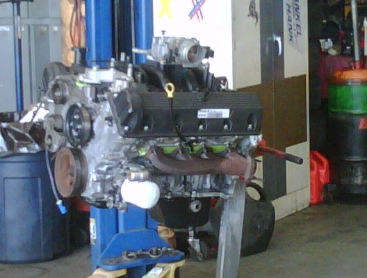 V8 engine on a stand in a garage, with tools and bins in the background