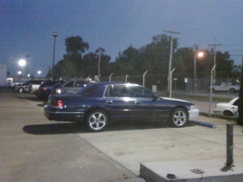 2005 Ford Crown Victoria - A dark blue sedan with a white front bumper is parked in a lot at dusk.