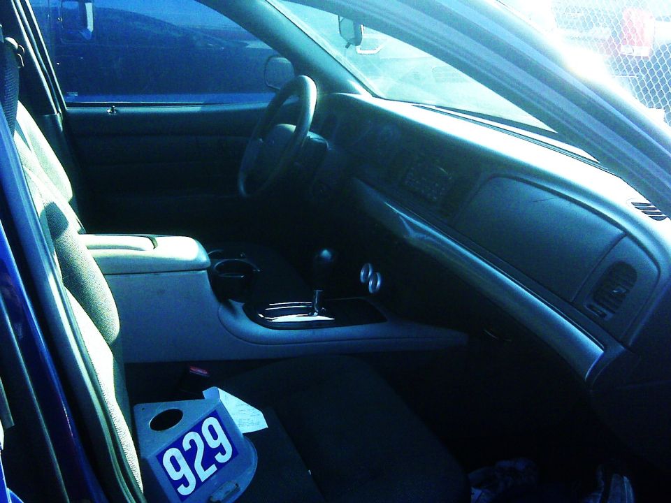 2005 Ford Crown Victoria interior showing dashboard, steering wheel, center console, and front seats. Blue tag with '929' is on the passenger seat