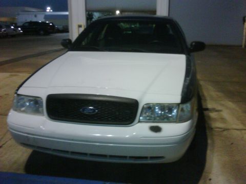 2005 Ford Crown Victoria - The front of a white 2005 Ford Crown Victoria is visible, a black grille and clear headlights.