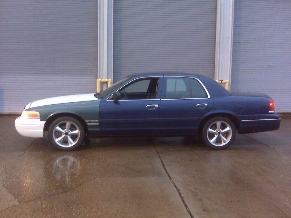 Side view of a blue and white sedan with aftermarket wheels parked in front of a garage door