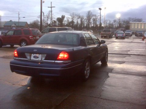 2005 Ford Crown Victoria - A dark blue Ford Crown Victoria is parked in a lot with other vehicles under a cloudy sky.