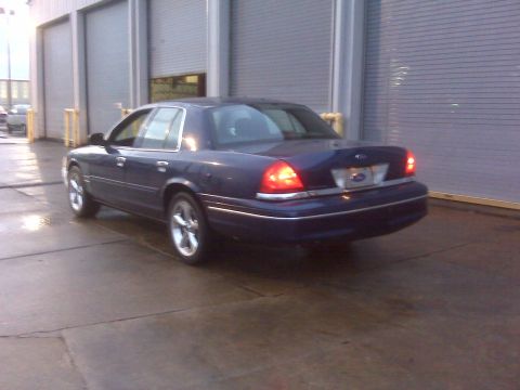 2005 Ford Crown Victoria - A dark blue sedan is parked on wet concrete in front of a large garage door.