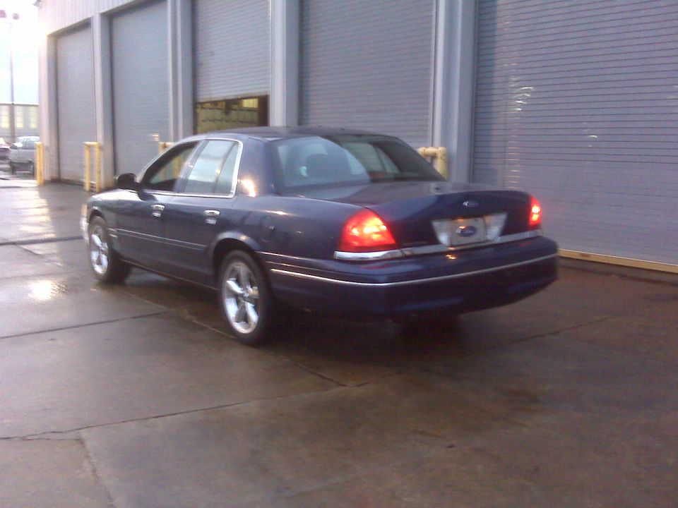 Dark blue sedan, rear 3/4 view, parked on wet concrete in front of a large garage door