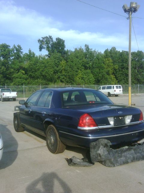 2005 Ford Crown Victoria - 2005 Ford Crown Victoria parked outside with damage to the front end and a detached bumper piece.