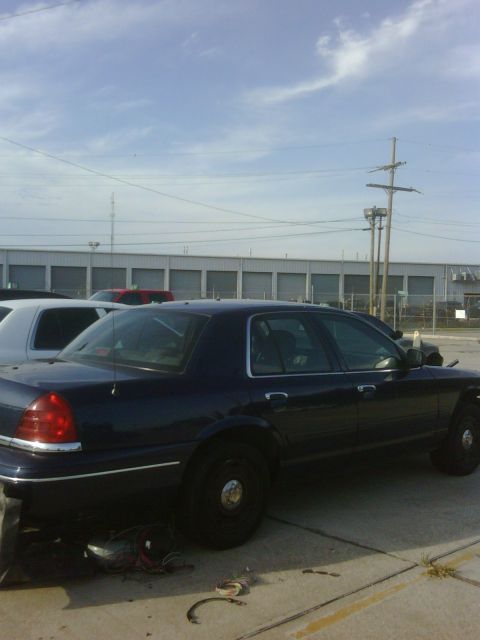 2005 Ford Crown Victoria - A dark blue 2005 Ford Crown Victoria sedan is parked on asphalt next to a white vehicle under a cloudy sky.