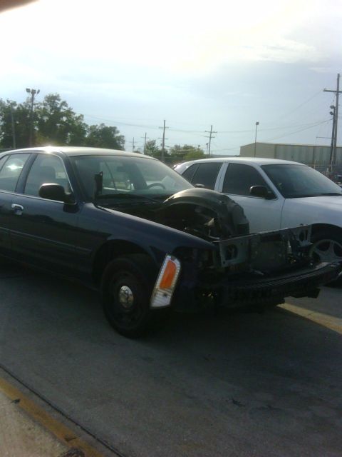 2005 Ford Crown Victoria - A dark blue 2005 Ford Crown Victoria is shown with its hood open and front end damaged, parked next to a white vehicle.
