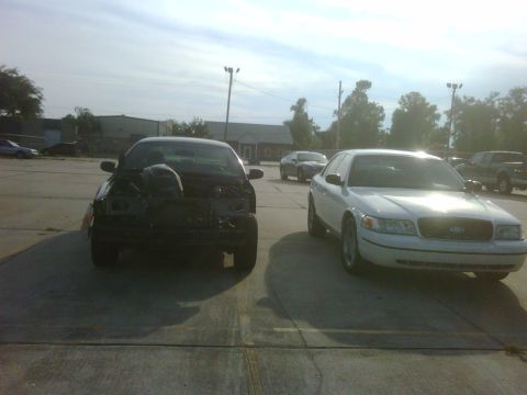 2005 Ford Crown Victoria - Two Ford Crown Victorias are parked outside, one appears to have front-end damage.