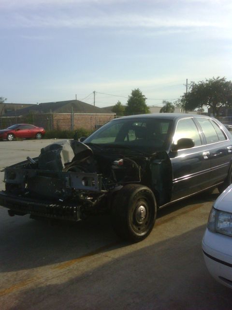 2005 Ford Crown Victoria - A dark sedan, possibly a 2005 Ford Crown Victoria, is parked outside with its front end disassembled.