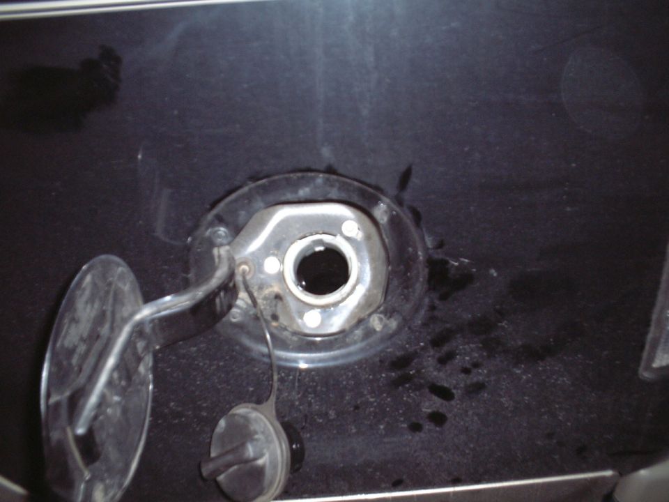 Open fuel filler neck with cap hanging by tether on dark painted panel