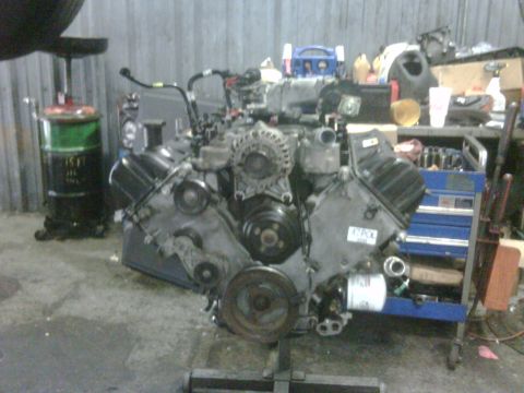 2005 Ford Crown Victoria - Engine assembly, likely a Ford modular V8, is mounted on an engine stand in a workshop.