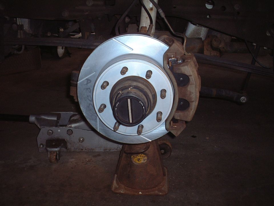 Front brake rotor, 8-lug hub with locking hubs, and caliper on jack stand under a truck.