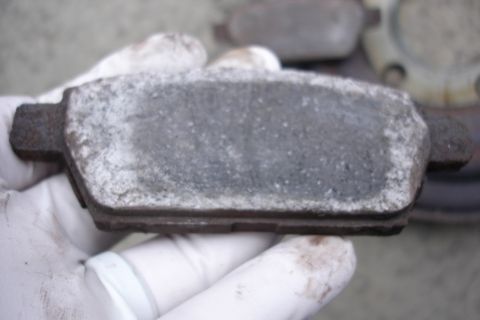 2006 Ford Fusion - A worn brake pad is held by gloved hands, showing significant wear and buildup.