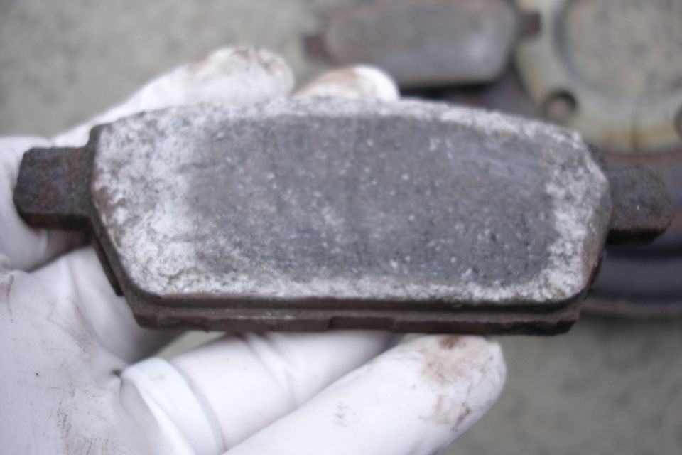 Worn brake pad held by gloved hands