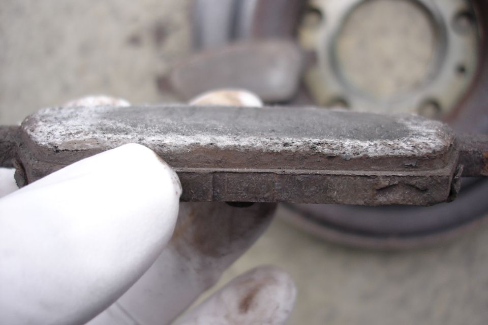 worn brake pad held by gloved hand, rotor visible in background