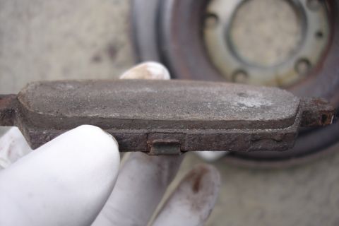 2006 Ford Fusion - A gloved hand holds a worn brake pad, showing the need for replacement. A brake rotor is visible behind it.