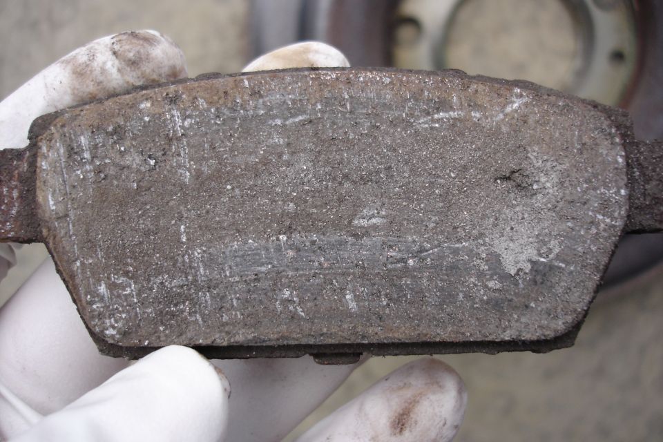 Worn brake pad held by gloved hands, showing scoring and dust
