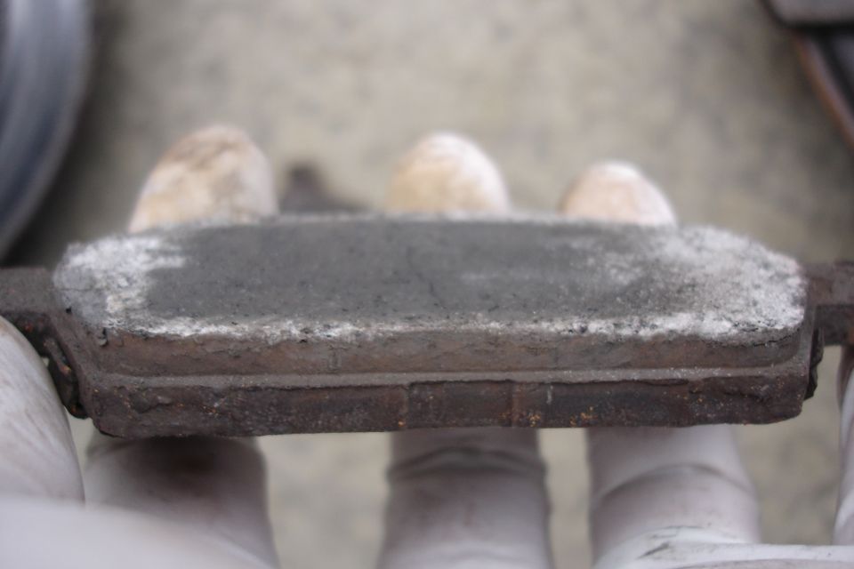 Close-up of a worn brake pad with dust and white residue