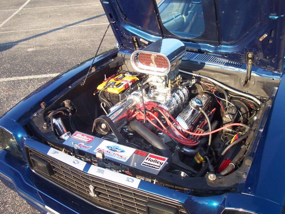 Blue car engine bay with chrome blower, scoop, red wires and racing decals