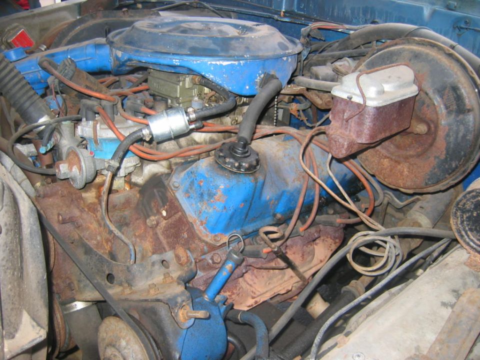 Worn blue Ford V8 engine with rusty exhaust and orange plug wires