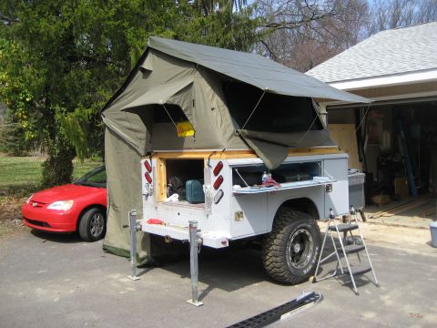 1996 Ford Bronco - A campsite setup a trailer with an extended rooftop tent and a red car parked beside it.