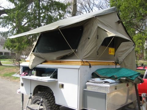 1996 Ford Bronco - This pop-up truck camper is set up with storage bins and a toolbox visible.
