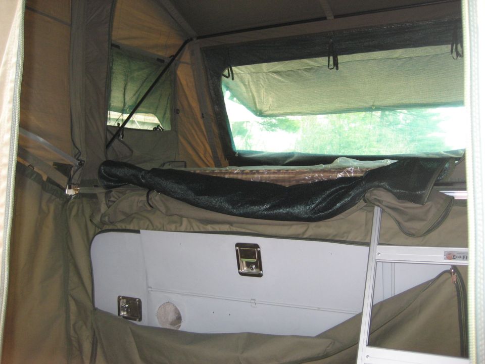 Interior of a pop-up camper tent with canvas walls, a bed platform, and storage compartments