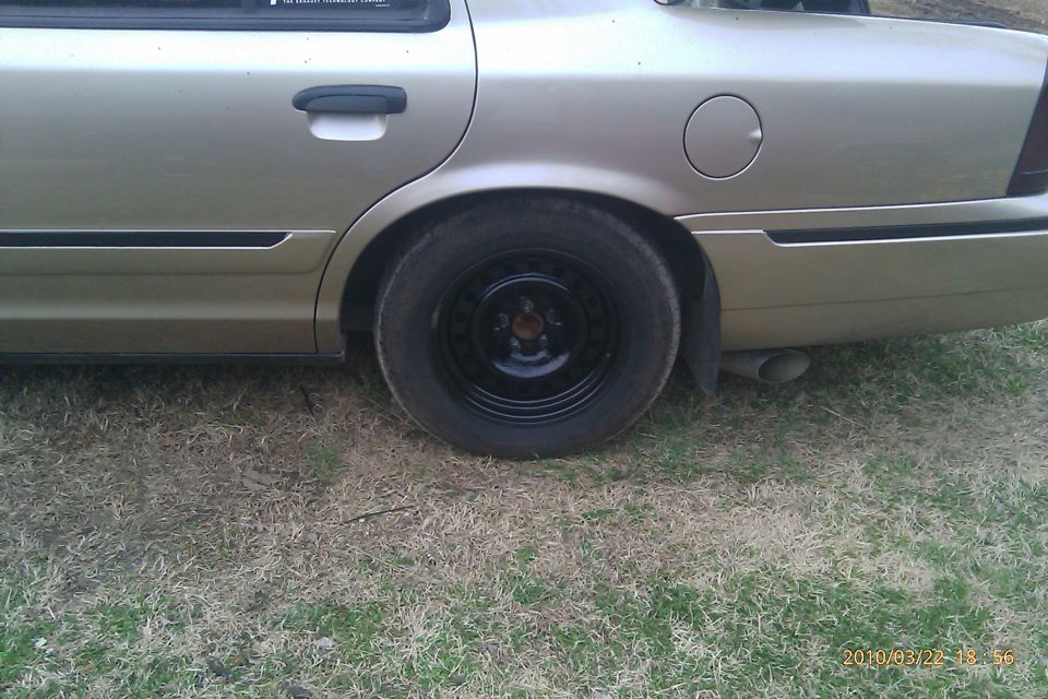 Gold sedan rear quarter panel, black steel wheel, exhaust pipe visible