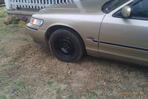 2000 Mercury Grand Marquis - This gold sedan is parked on dry grass next to a white railing. The front passenger side is visible.
