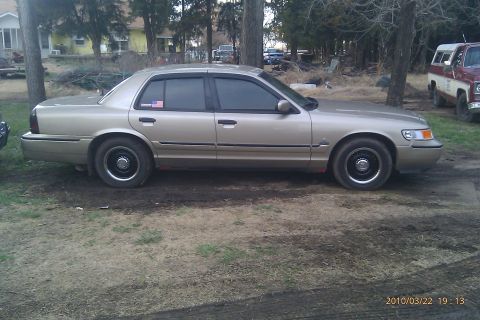 2000 Mercury Grand Marquis - A gold 2000 Mercury Grand Marquis sedan is seen from the side in an outdoor setting.