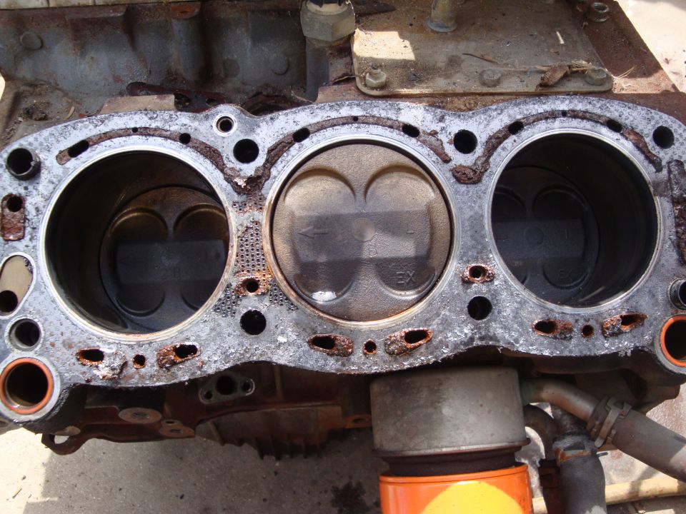 Close-up of an engine block showing three pistons and cylinder bores. Some corrosion is visible