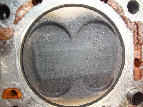 1989 Ford Taurus - The top of a piston within an engine cylinder, marked by carbon deposits and indentations for valves.