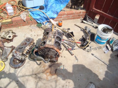 1989 Ford Taurus - Engine block and various engine parts are laid out on a concrete surface, suggesting a repair or rebuild in progress.