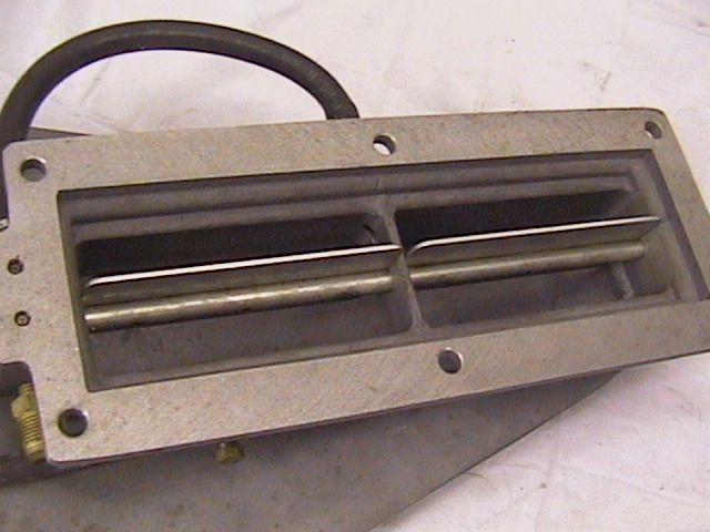Close-up of a metal carburetor component with two internal flaps and a black hose attached