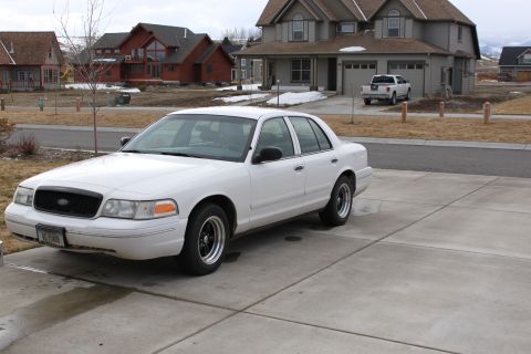 1998 Ford Crown Victoria - A white 1998 Ford Crown Victoria is parked in a suburban driveway with houses in the background.