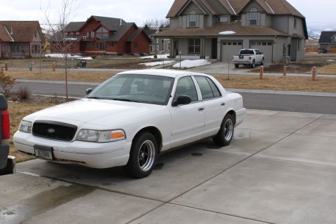 1998 Ford Crown Victoria - A white 1998 Ford Crown Victoria sedan is parked in a driveway with houses in the background.