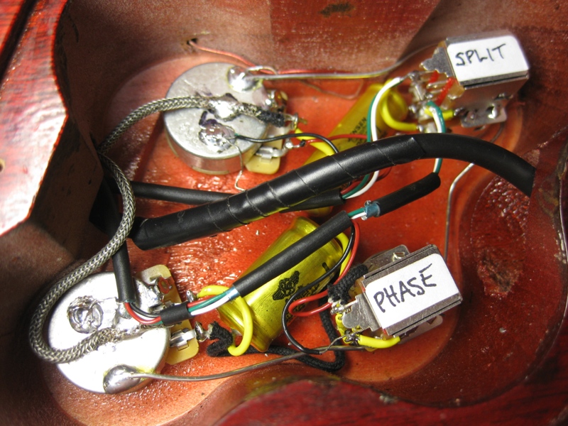 Guitar wiring cavity with potentiometers, capacitors, and switches labeled "SPLIT" and "PHASE"