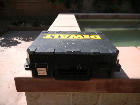 1997 Ford Ranger - A scuffed black DeWalt plastic tool case with yellow logo lying upside down on the tiled coping of a backyard pool, with a block wall and g…