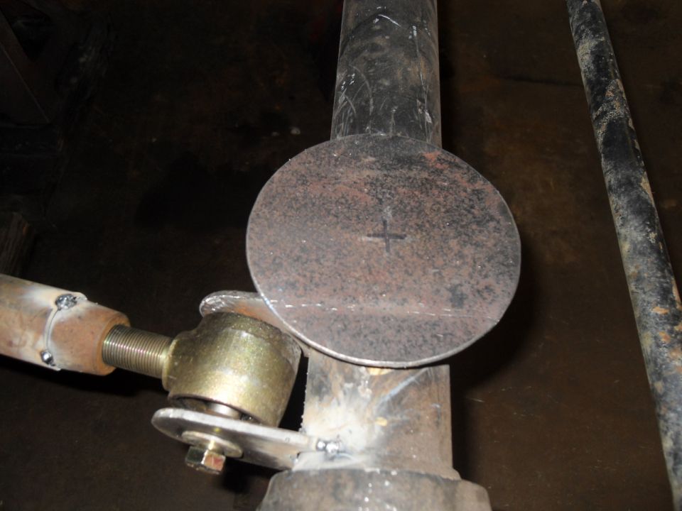 Close-up of a metal disc with a crosshair marked on it, welded to a pipe with a threaded rod assembly attached