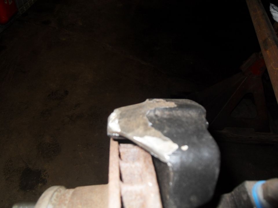 Close-up of a rusty metal part, possibly a suspension component, held by a vise
