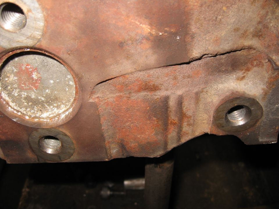 Close-up of a heavily rusted engine block casting with several bolt holes and a visible crack