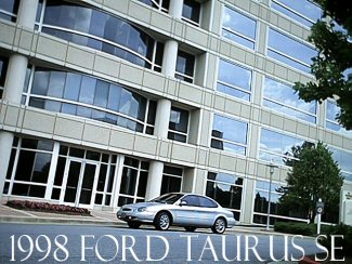 1998 Ford Taurus - A silver 1998 Ford Taurus sedan is seen parked in front of a modern building with large glass windows.