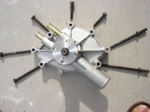 1992 Ford Bronco - Water pump part with bolts arranged radially on a concrete surface.