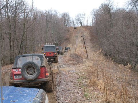 1985 Ford Bronco - Off-road vehicles navigate a muddy trail through a wooded area.