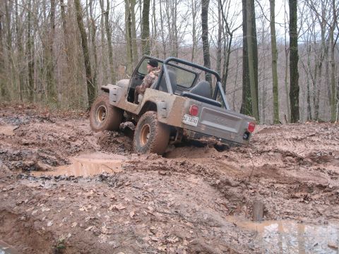 1985 Ford Bronco - A Jeep CJ-7 tackles a challenging muddy off-road course, demonstrating its off-road capabilities.