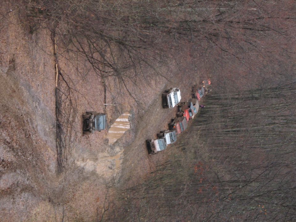 Multiple off-road vehicles driving in a line on a muddy, wooded trail
