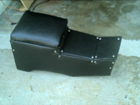 1989 Ford Bronco - A shop-built center console sits on a concrete garage floor, wrapped in black vinyl with a padded lid and visible upholstery screws along t…