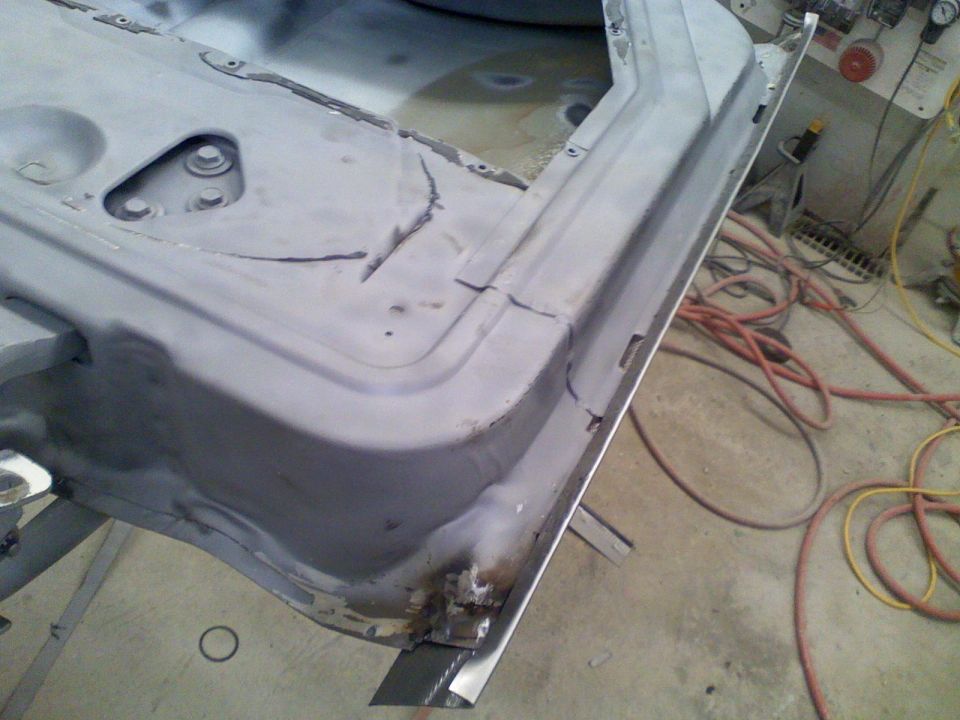 Close-up of a vehicle's lower door frame and rocker panel undergoing repair, showing primer and rust