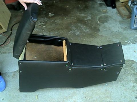 1989 Ford Bronco - removed black vinyl center console with its hinged armrest lid open, sitting on a concrete garage floor.